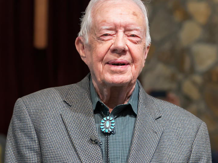 President Carter wears a gray houndstooth jacket and turquoise bolo tie.