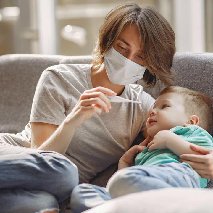 A mother wearing a face mask taking her young son's temperature.