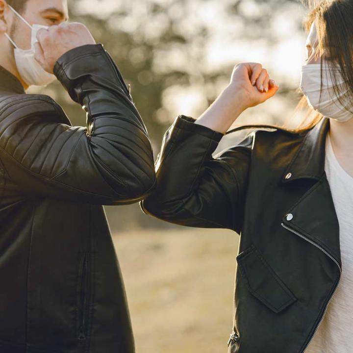 Two friends wearing face masks bumping elbows.